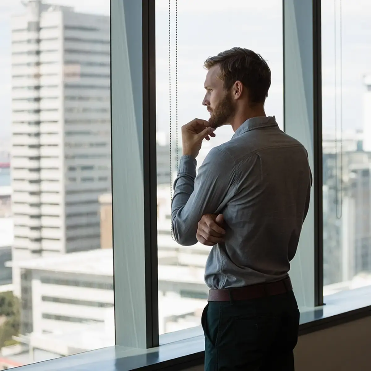 Corporate executive looking out office window, highlighting the need for executive protection strategies against online and physical threats.